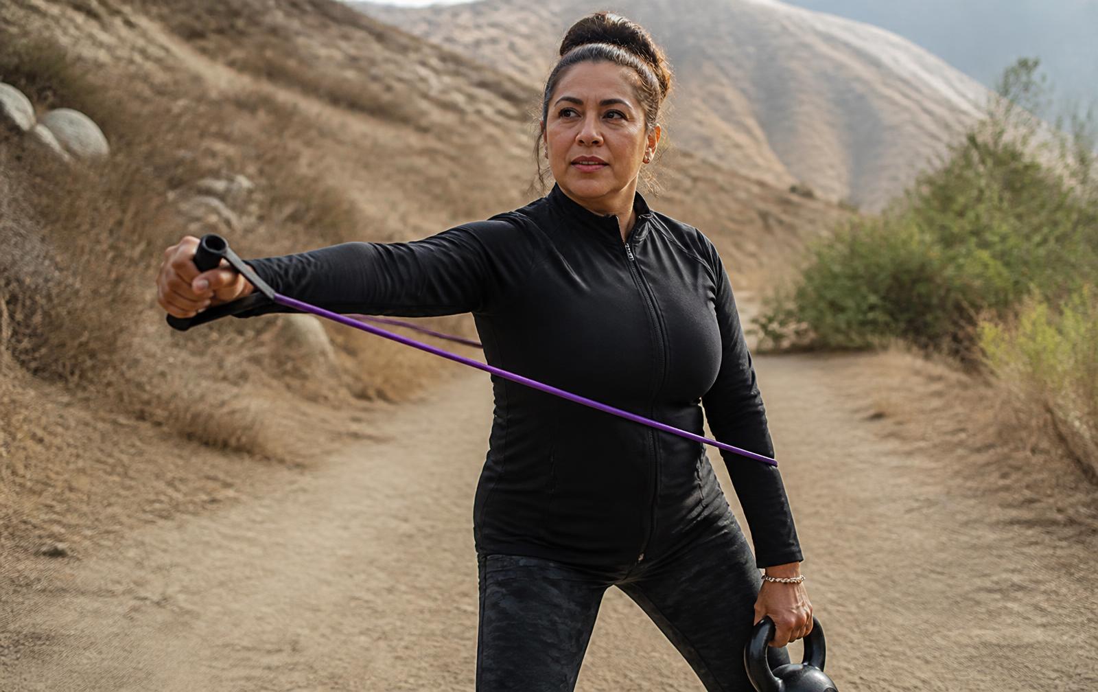 A woman training outdoors with a weighted pack while a coach guides her